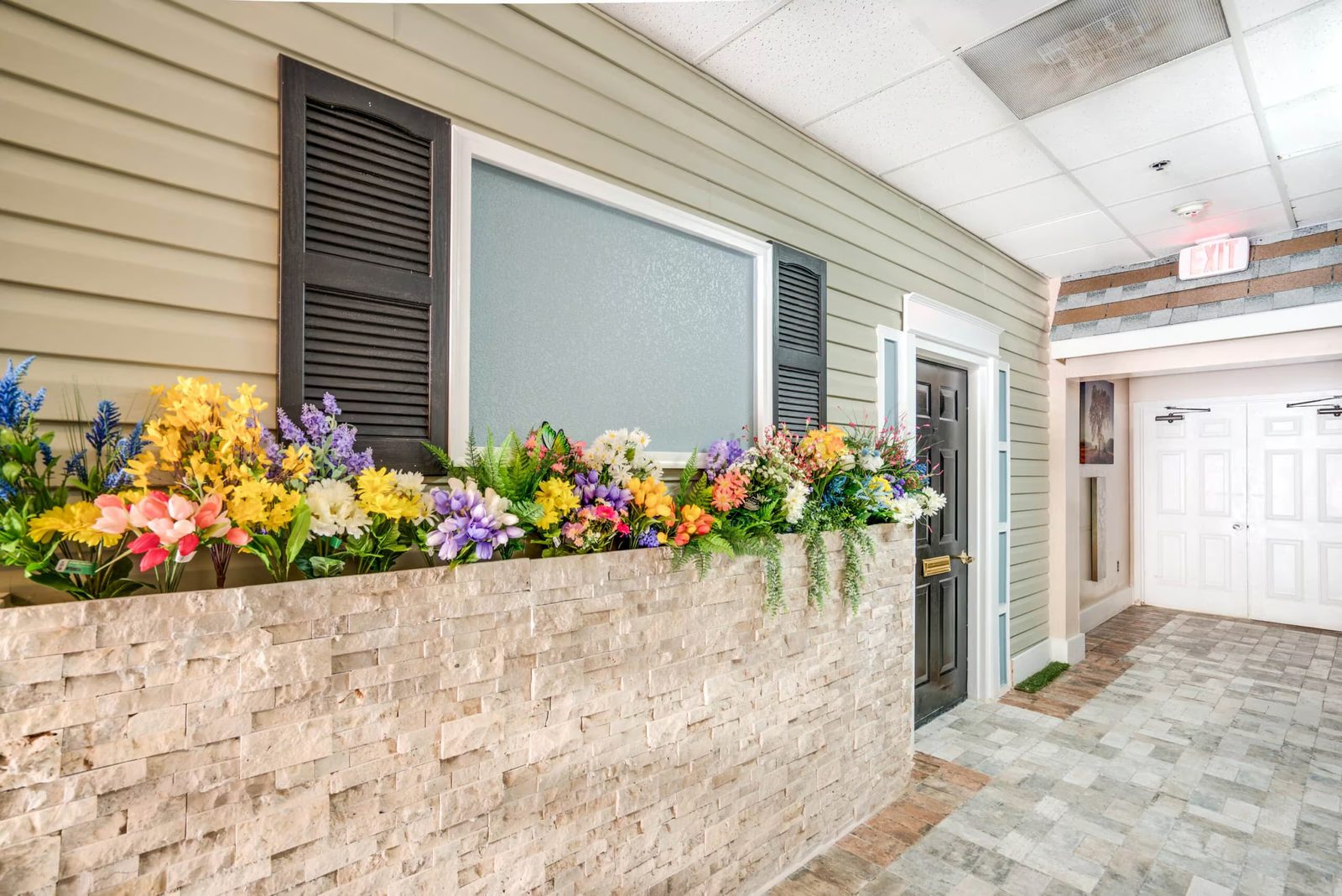 Stone planter of colorful flowers along a house-style front in the indoor neighborhood at Colonial Gardens assisted living, Lauderhill