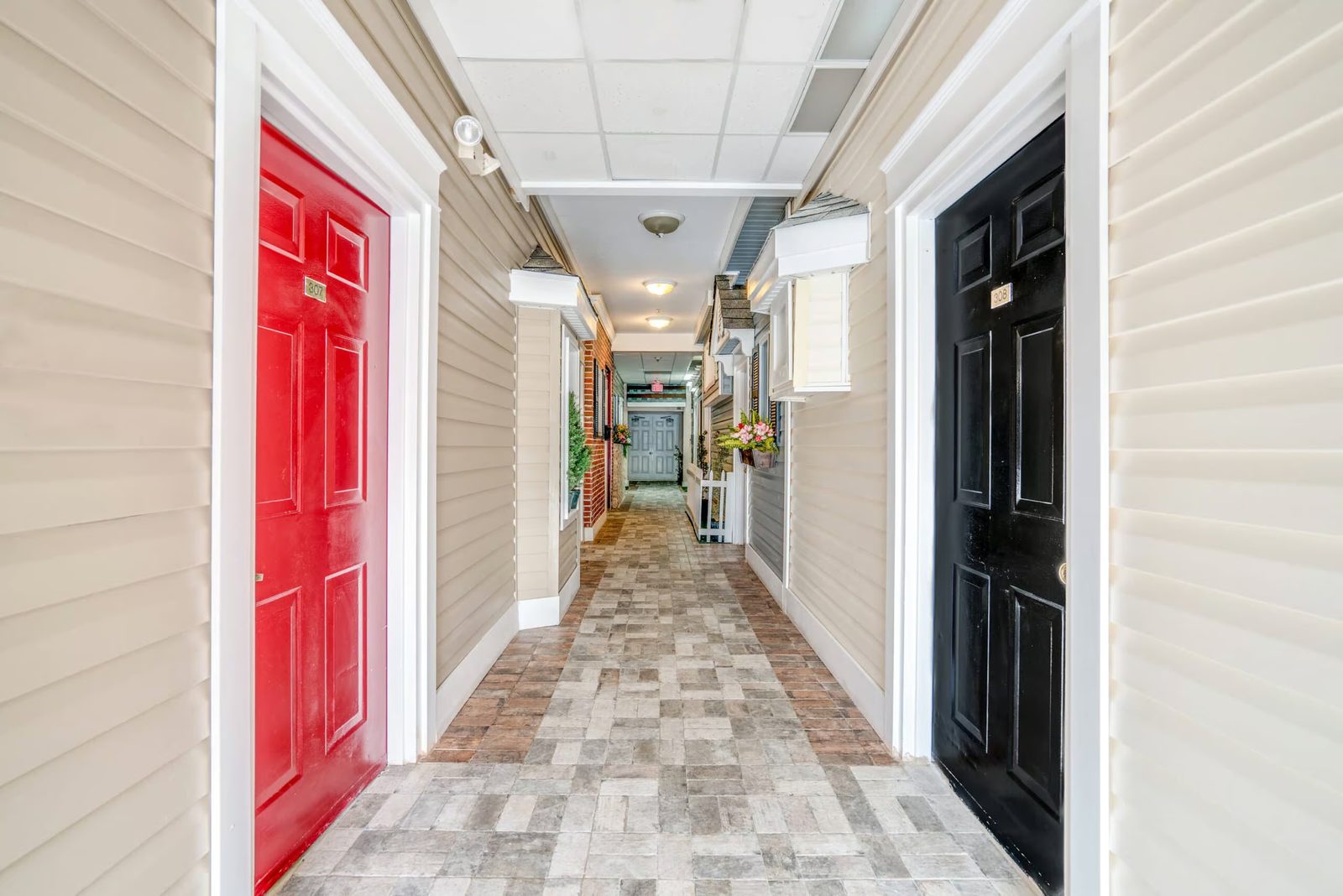 Red and black front doors with flower boxes along a memory care hallway at Colonial Gardens Residences, Lauderhill, FL