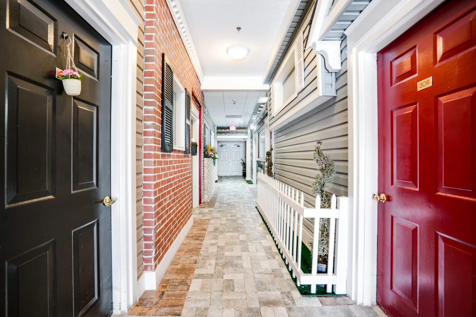 Memory care hallway designed like a neighborhood street, with a brick front, shutters and a red front door, at Colonial Gardens Residences in Lauderhill, Broward County